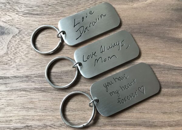 Engraved metal keychains with heartfelt messages on a wooden surface. Perfect for meaningful gifts or keepsakes.