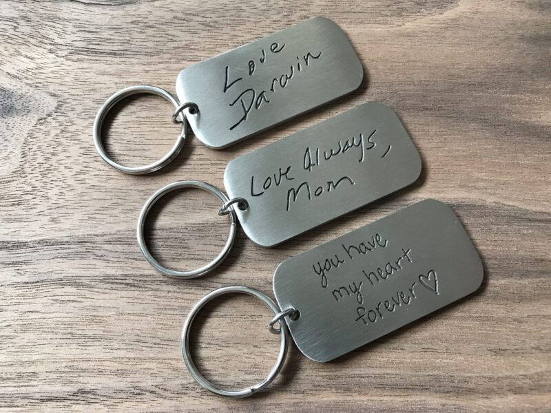 Engraved metal keychains with heartfelt messages on a wooden surface. Perfect for meaningful gifts or keepsakes.