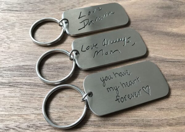 Engraved metal keychains with personalized messages on a wooden surface.