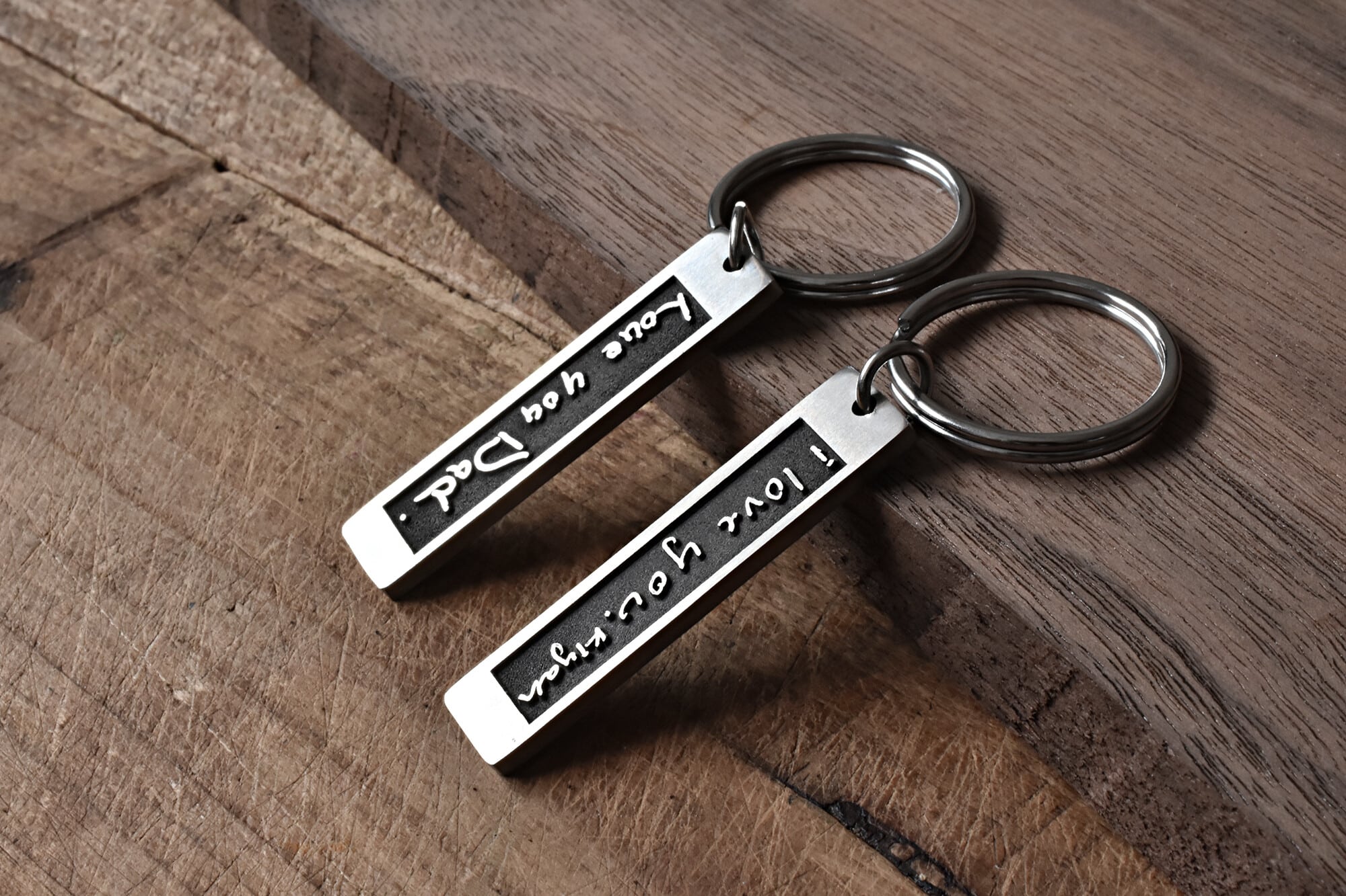 Two metal keychains engraved with Love You, Dad on a wooden surface, perfect for Father's Day gift.