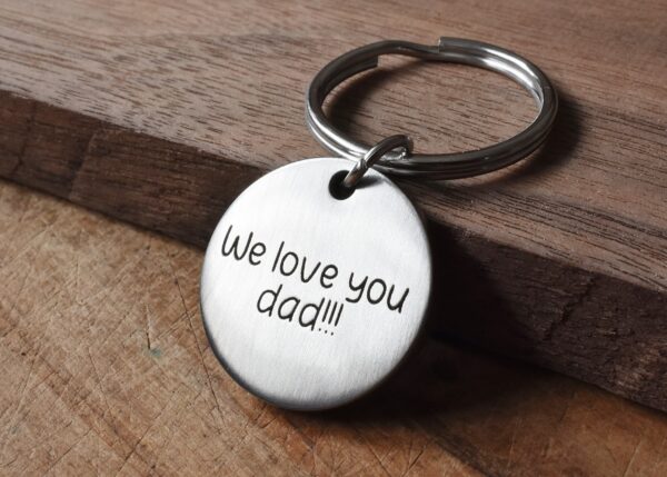 Silver keychain with engraved message We love you dad!!! resting on a wooden surface, perfect Father's Day gift.