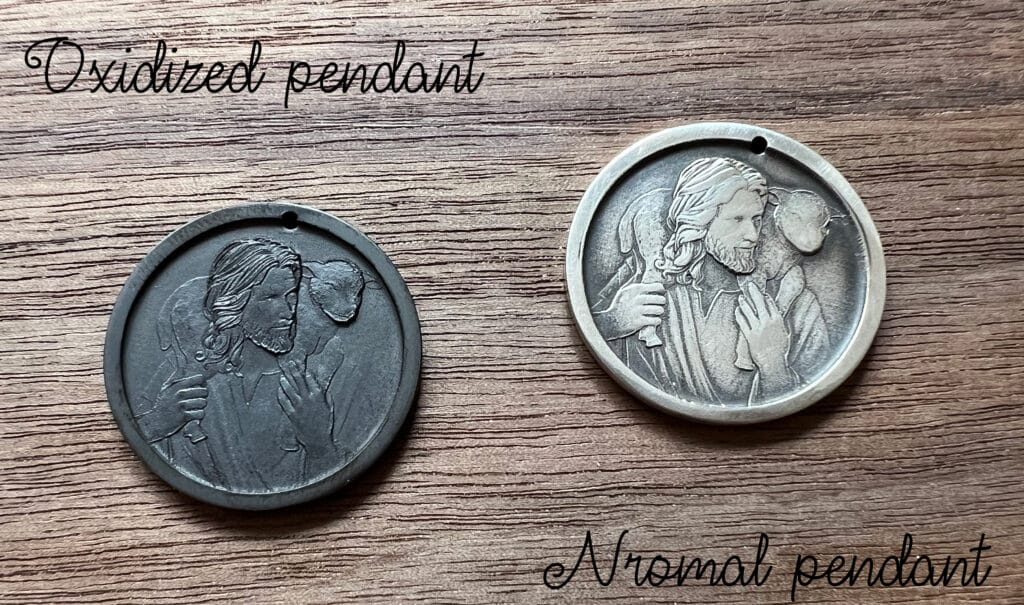 Oxidized and normal pendants on wood, both featuring a religious figure with a lamb on the shoulder.