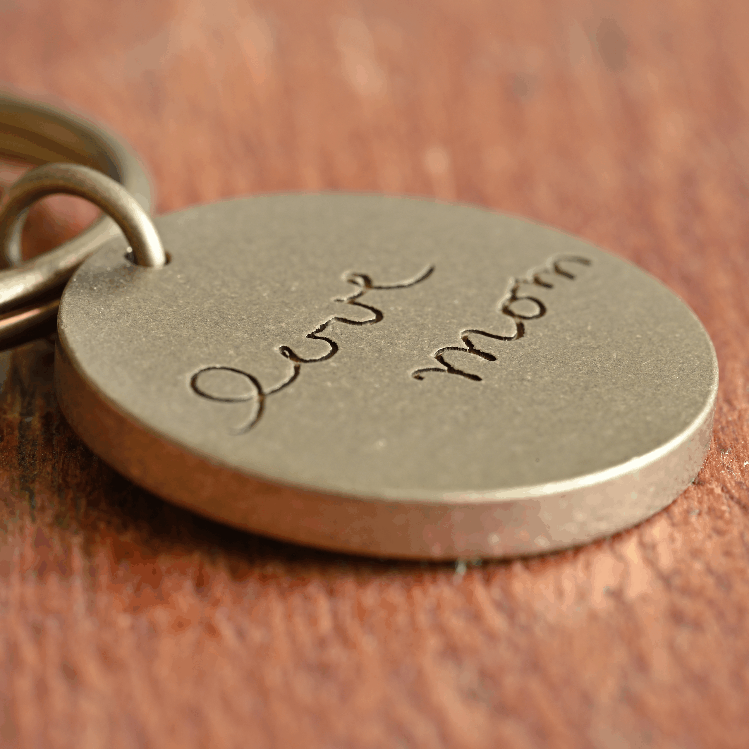 Engraved metal keychain reading love mom on wooden surface, symbolizing affection and appreciation.