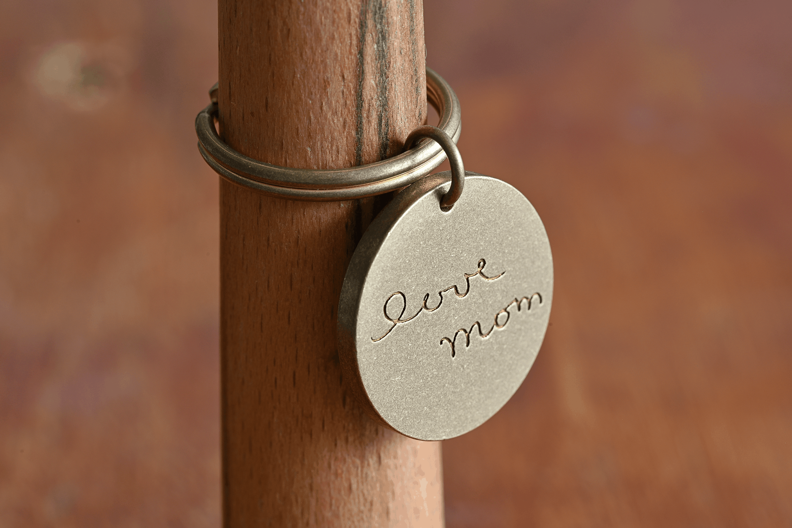 Engraved metal keychain with love mom hanging from a wooden pole, perfect personalized gift for Mother's Day.