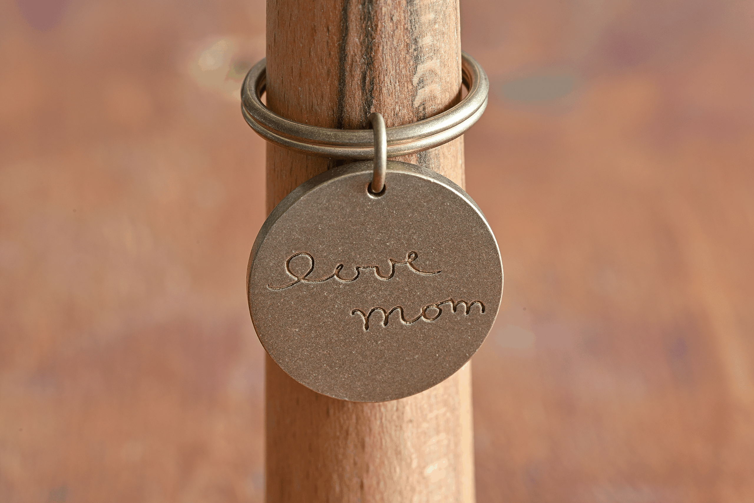 Engraved metal charm on ring holder with Love Mom inscription, perfect for jewelry or gift categories.