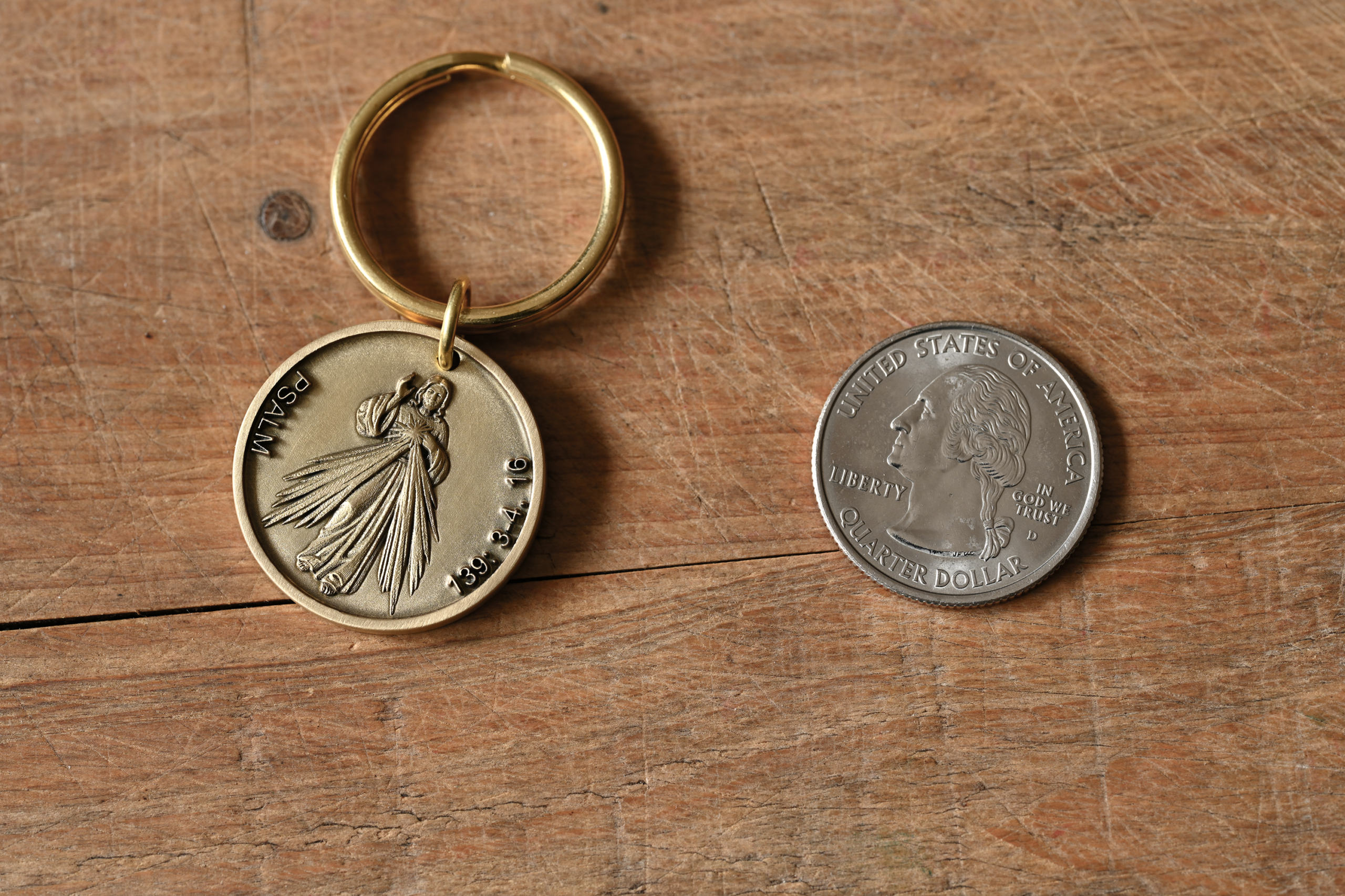 Personalized Keychain medallion with religious engraving next to a US quarter on wooden surface.