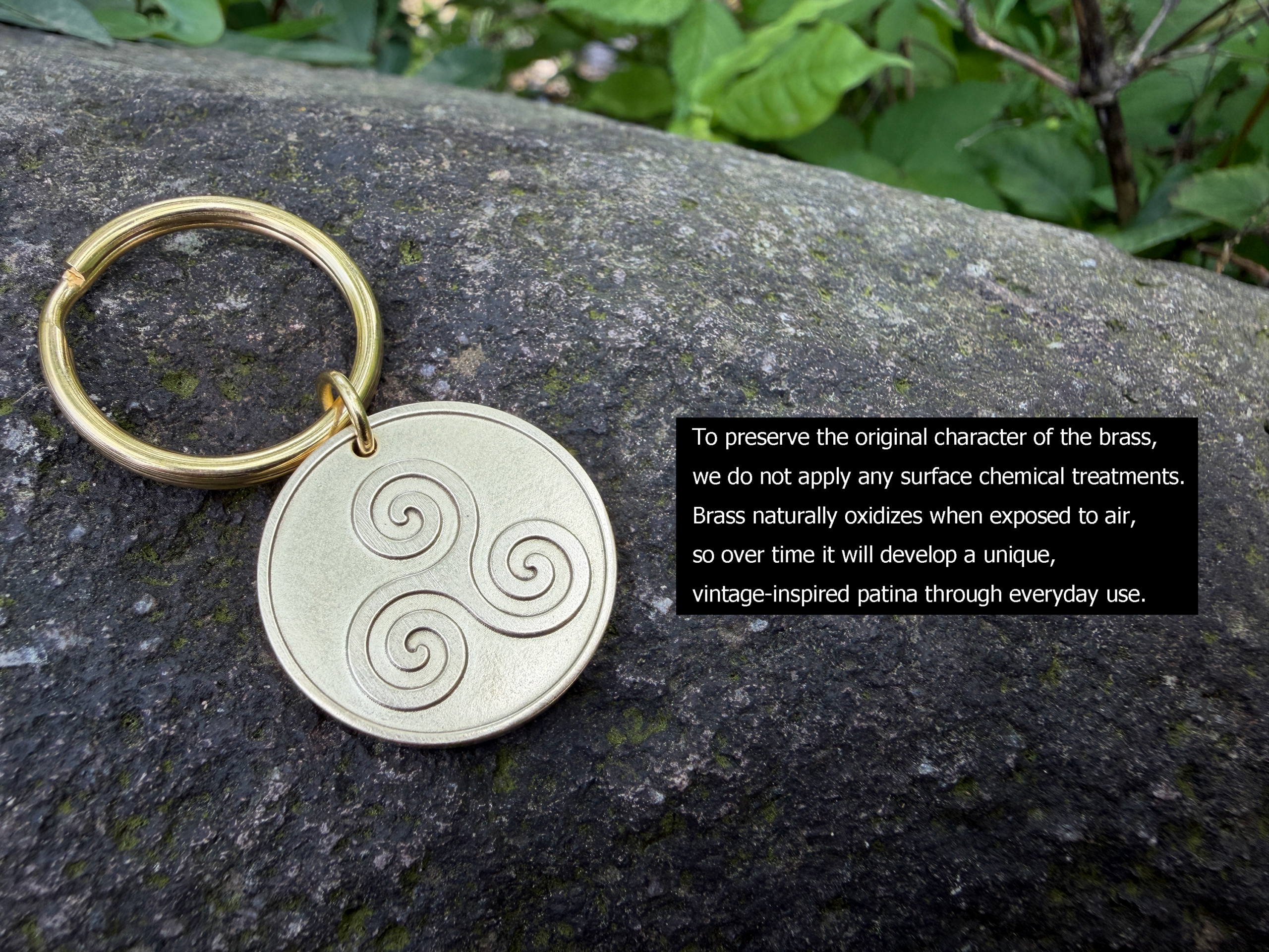 Brass keychain with triskelion engraving on a rock background, highlighting natural oxidation for patina development.