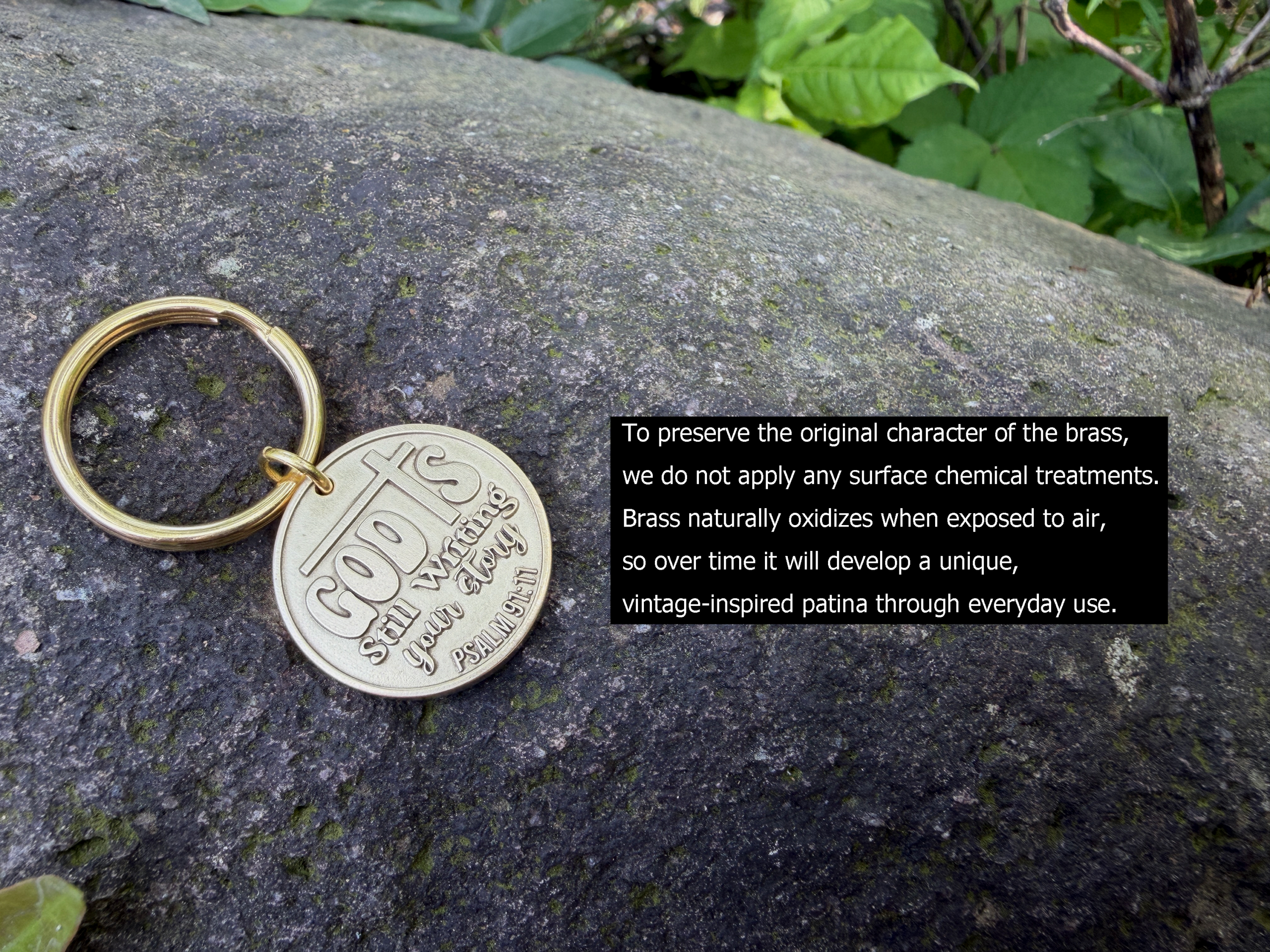 Brass keychain on rock engraved with God's still writing your story. Psalm 139:16 and oxidization message.