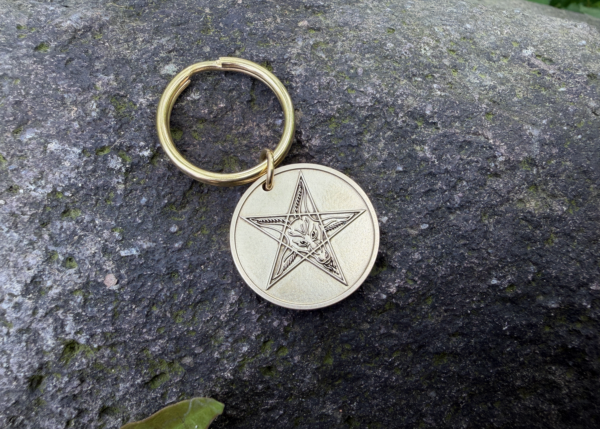 Gold keychain with Baphomet pentagram engraving on stone background.