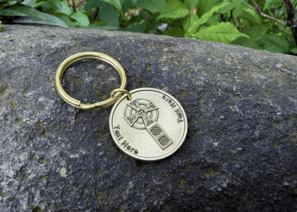 Gold keychain with Celtic cross design on stone surface outdoors. Text space available for personalization.