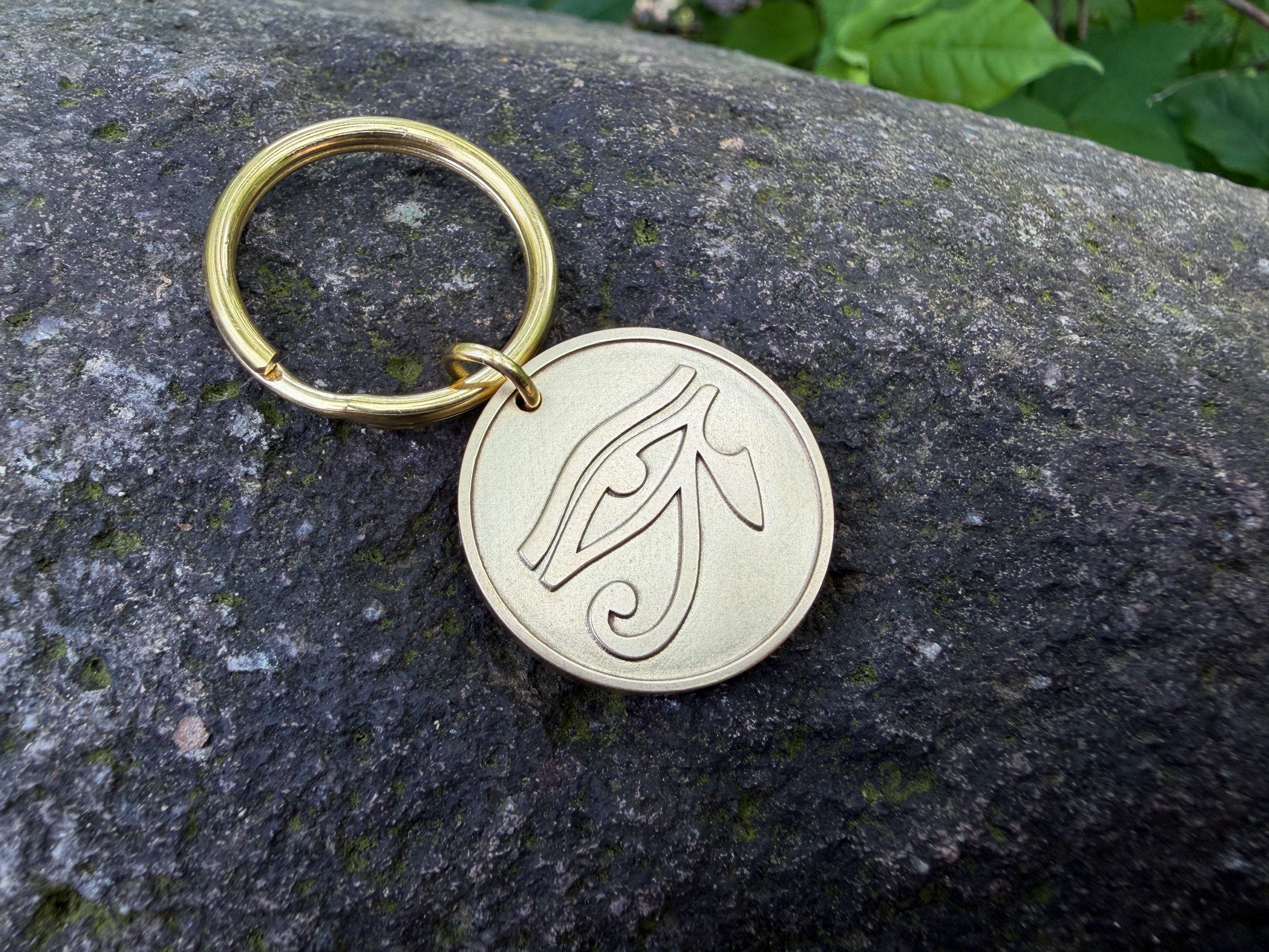 Gold keychain with Eye of Horus engraving resting on a textured stone surface.