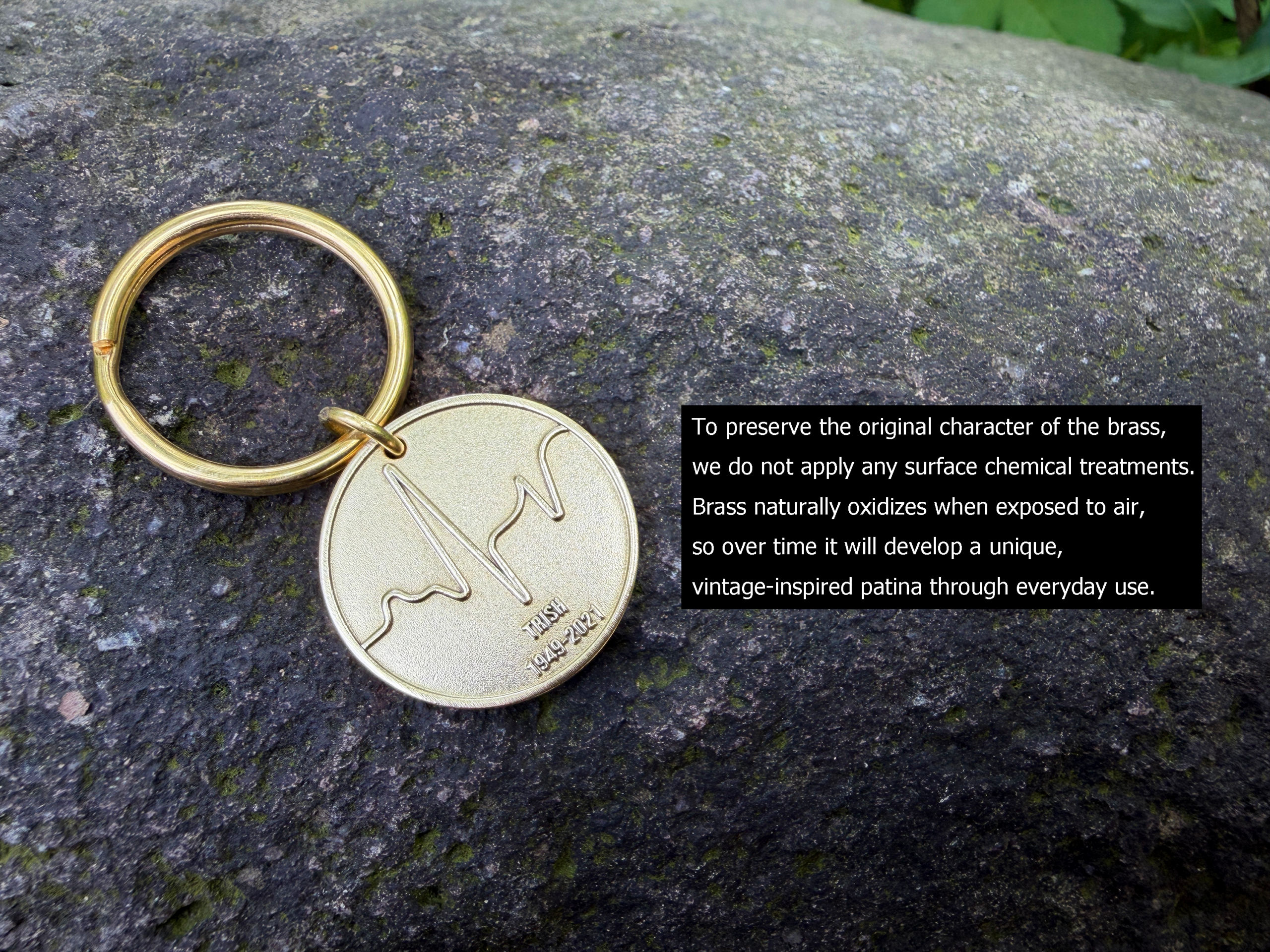Brass keychain on a rock with engraved soundwave and text Inis E 1949-2021, highlighting natural oxidation process.