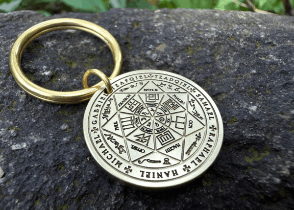 Ancient talisman keychain with intricate symbols and names on a stone background.