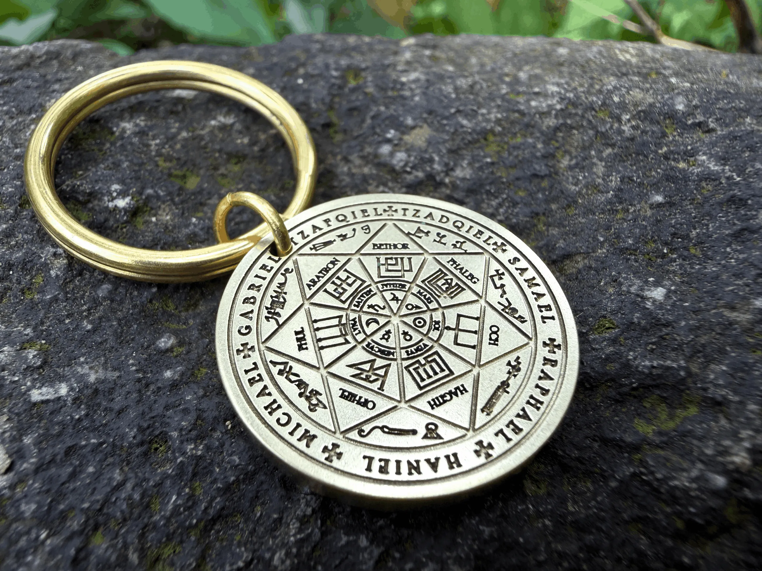 Brass keychain with Archangel Sigil engraved on a circular pendant, resting on a stone surface.