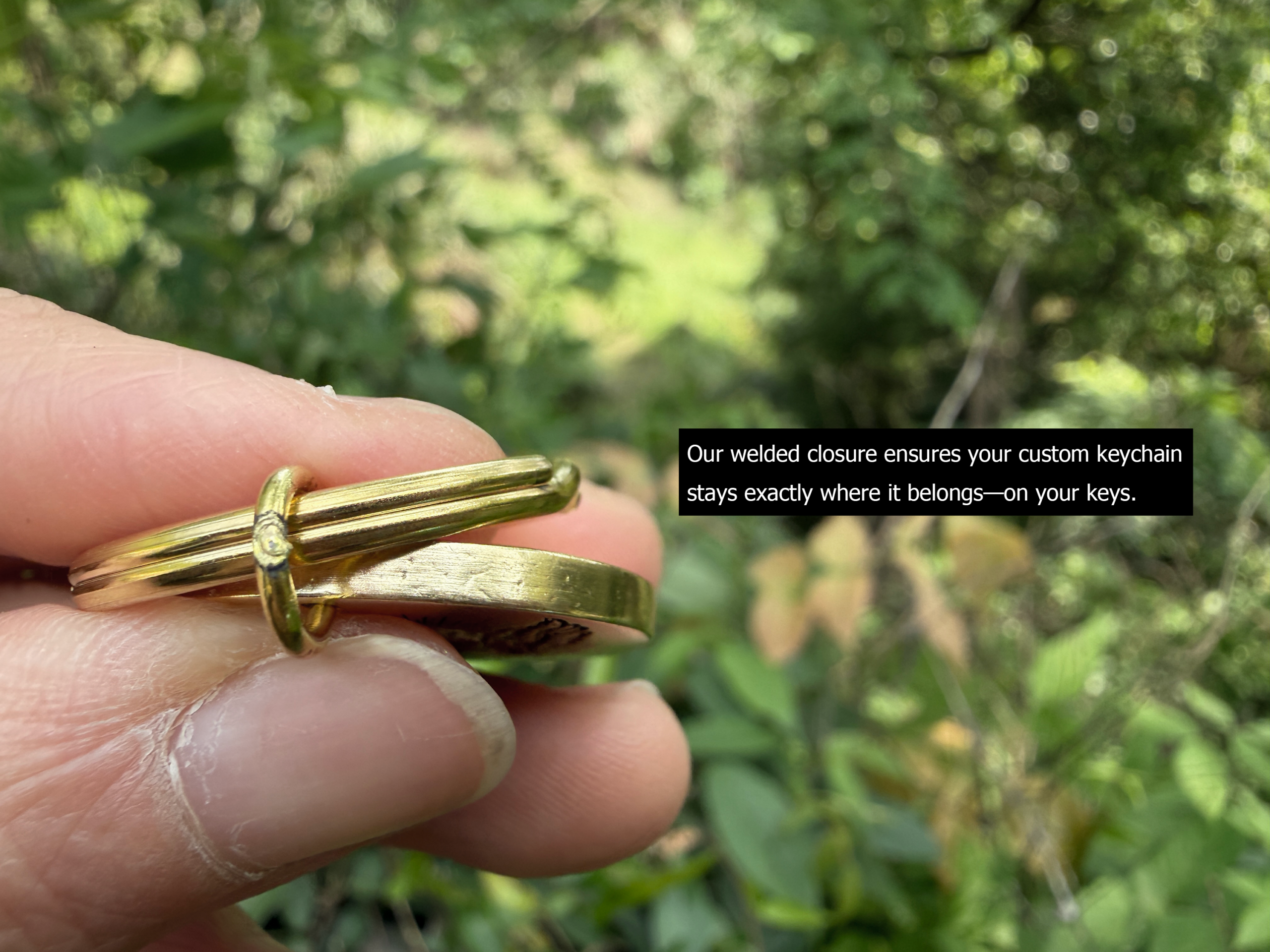 Close-up of a sturdy keychain with welded closure, held by fingers, ensuring keys are secure; green foliage background.