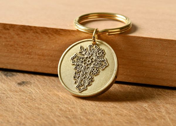 Gold keychain with a circular medallion featuring an embossed floral cross design