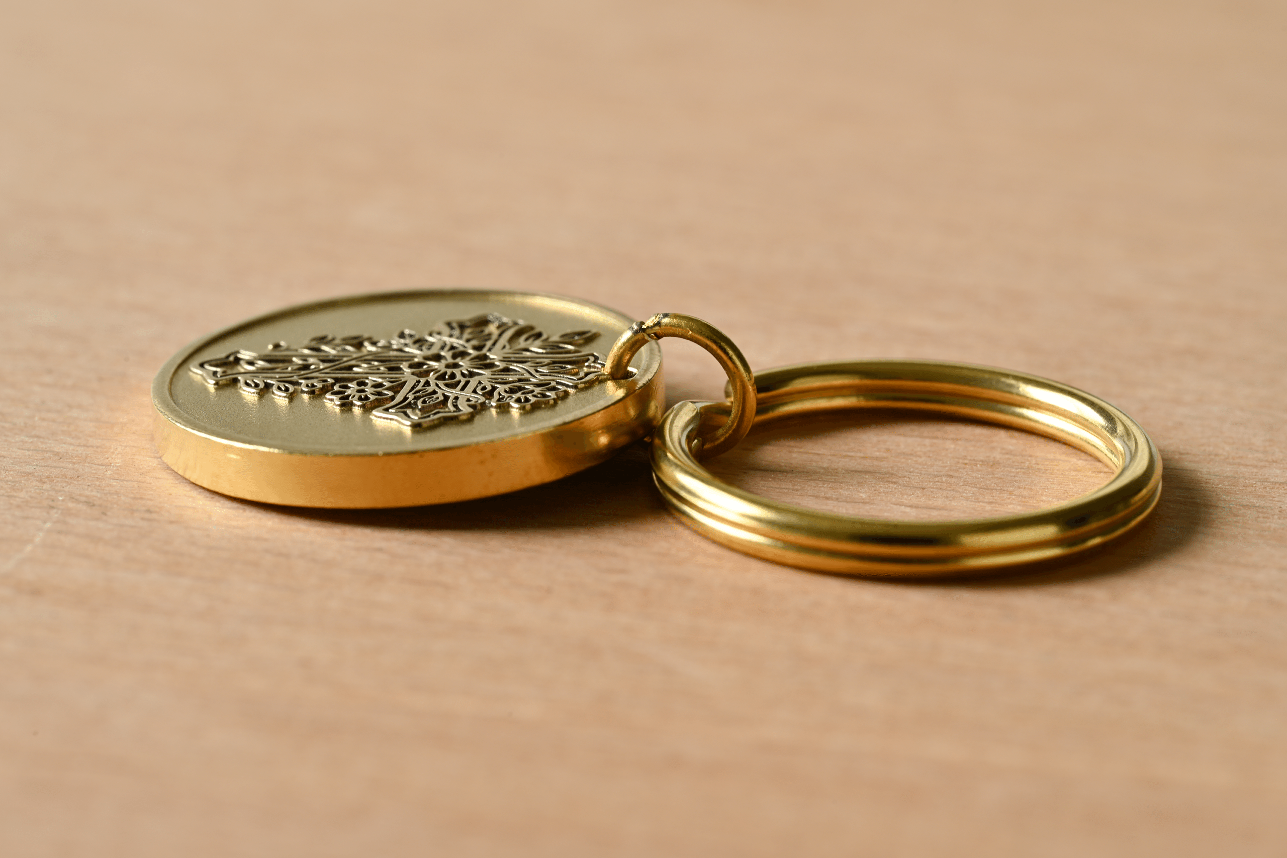 Gold-colored keychain with an intricate embossed medallion on a wooden surface