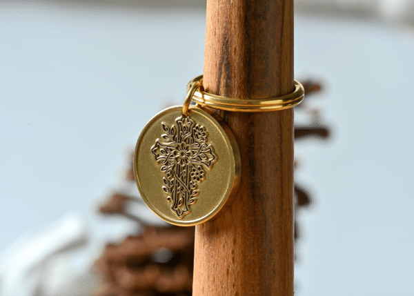 Gold circular pendant featuring an intricate embossed floral cross design
