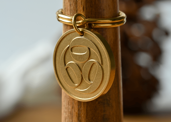 Gold circular keychain with a stylized 69 design hanging on a wooden post