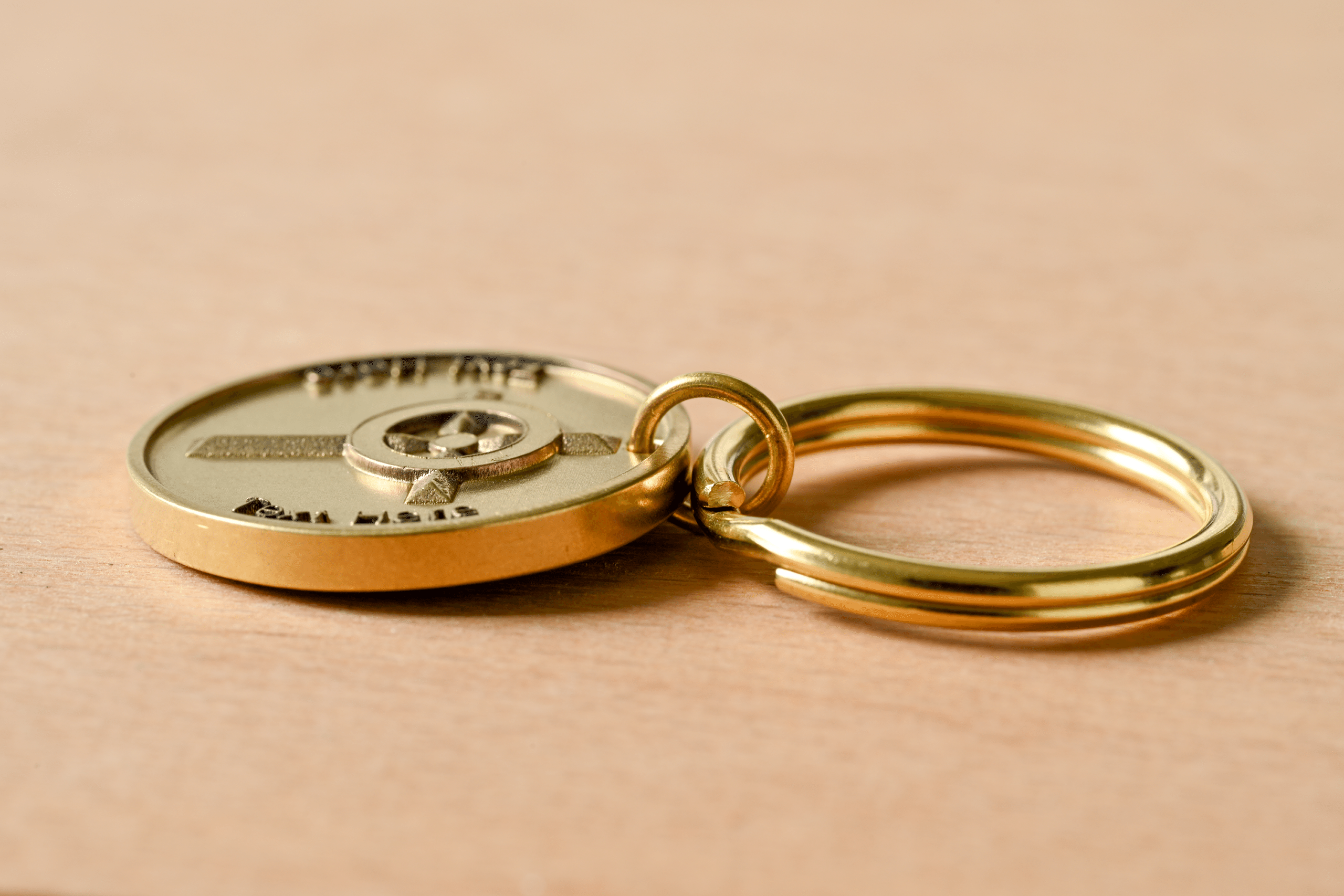 Gold medallion keychain engraved with "STAY SAFE" and "BE WELL" on a wooden surface