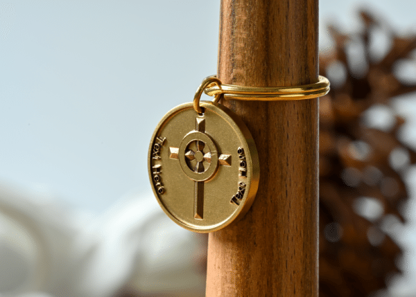 Gold circular keychain featuring a central cross design and customizable text placeholders on each side