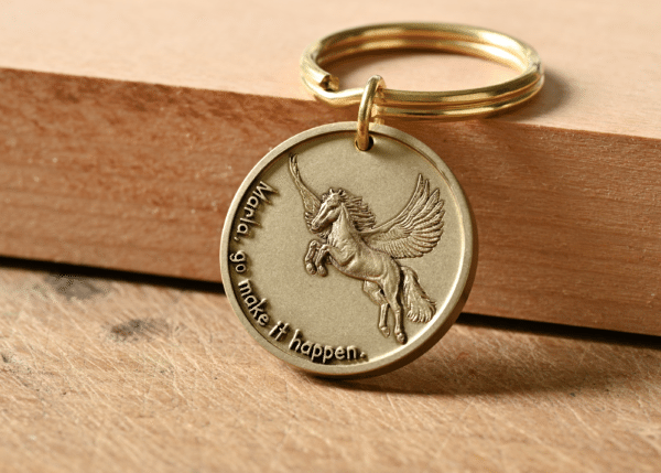 Gold circular keychain with an embossed Pegasus and the text: Marla, go make it happen