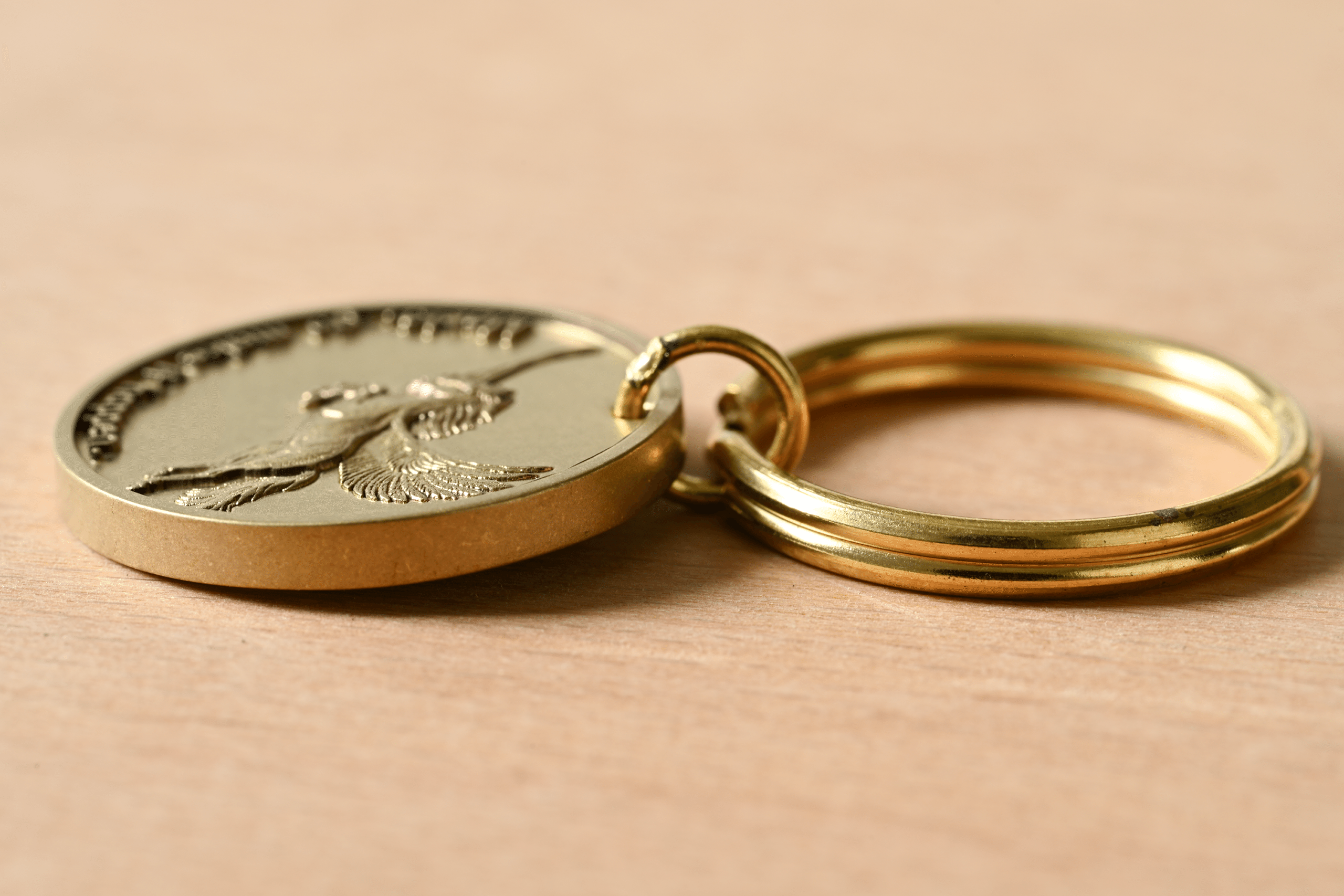Gold keychain with a round medallion featuring an embossed bird in flight