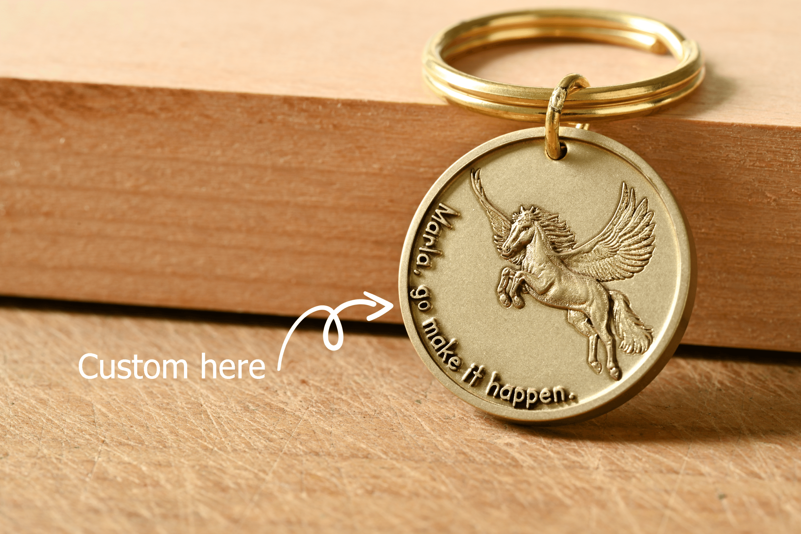 Gold keychain tag with an embossed Pegasus and customizable text. An arrow points to the text: Custom here