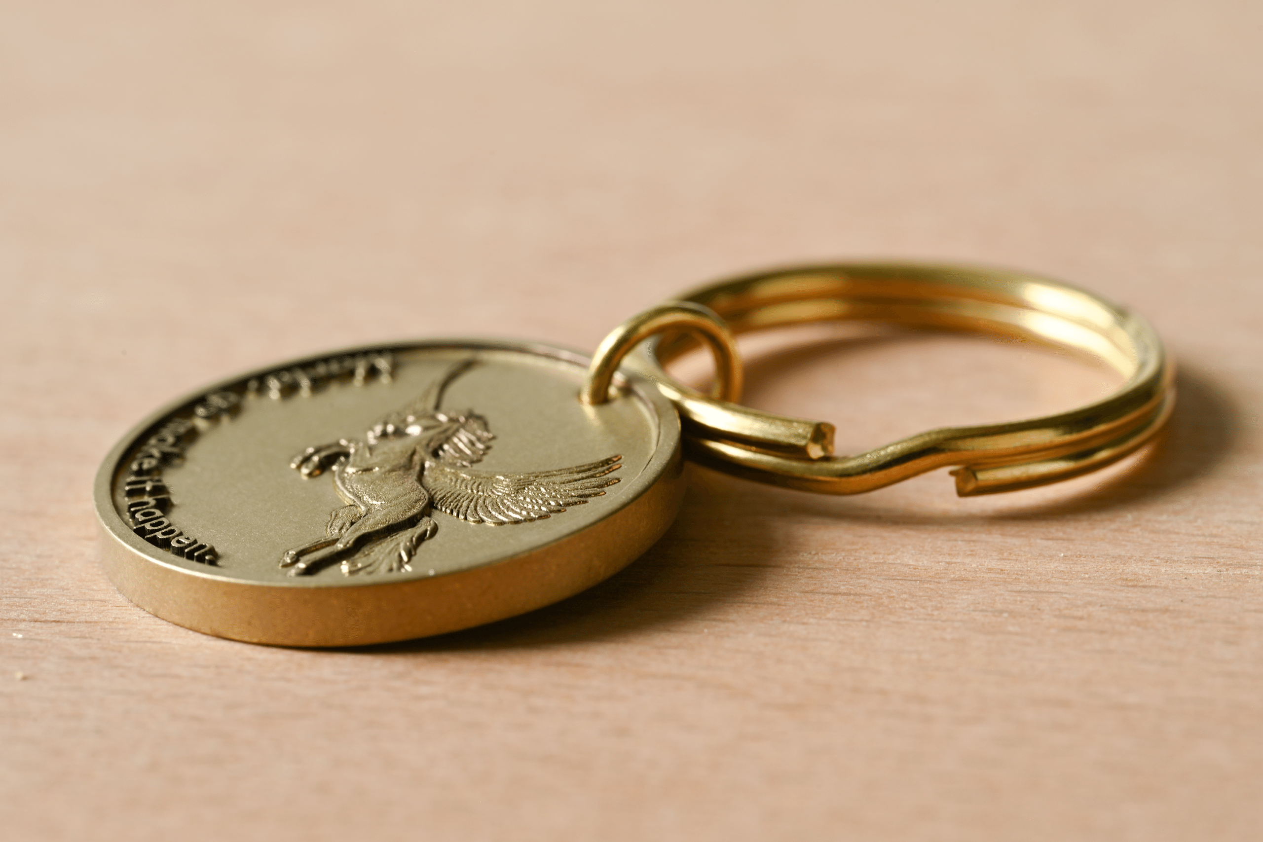 Gold-colored keychain medallion with an embossed winged horse and the text Make it happen