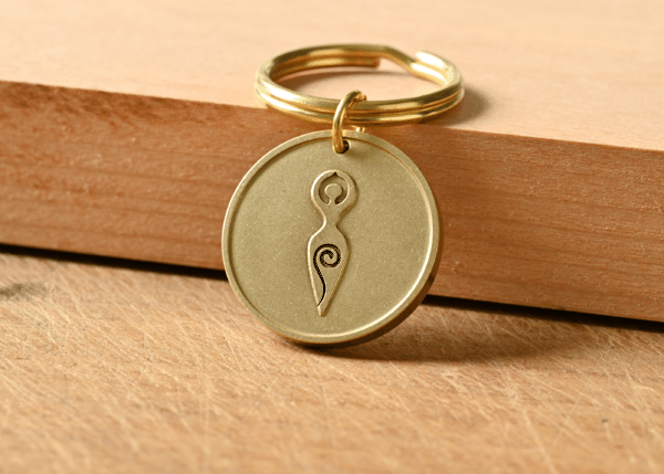 Brass keychain tag engraved with a Spiral Goddess symbol resting on a wooden surface
