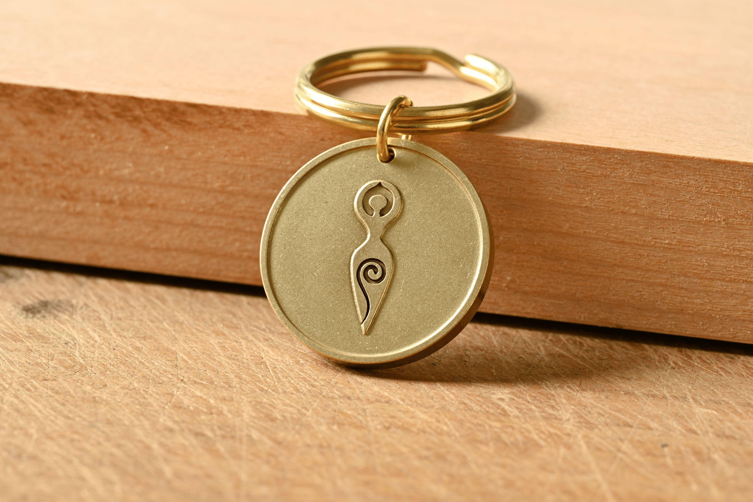 Brass keychain tag engraved with a Spiral Goddess symbol resting on a wooden surface