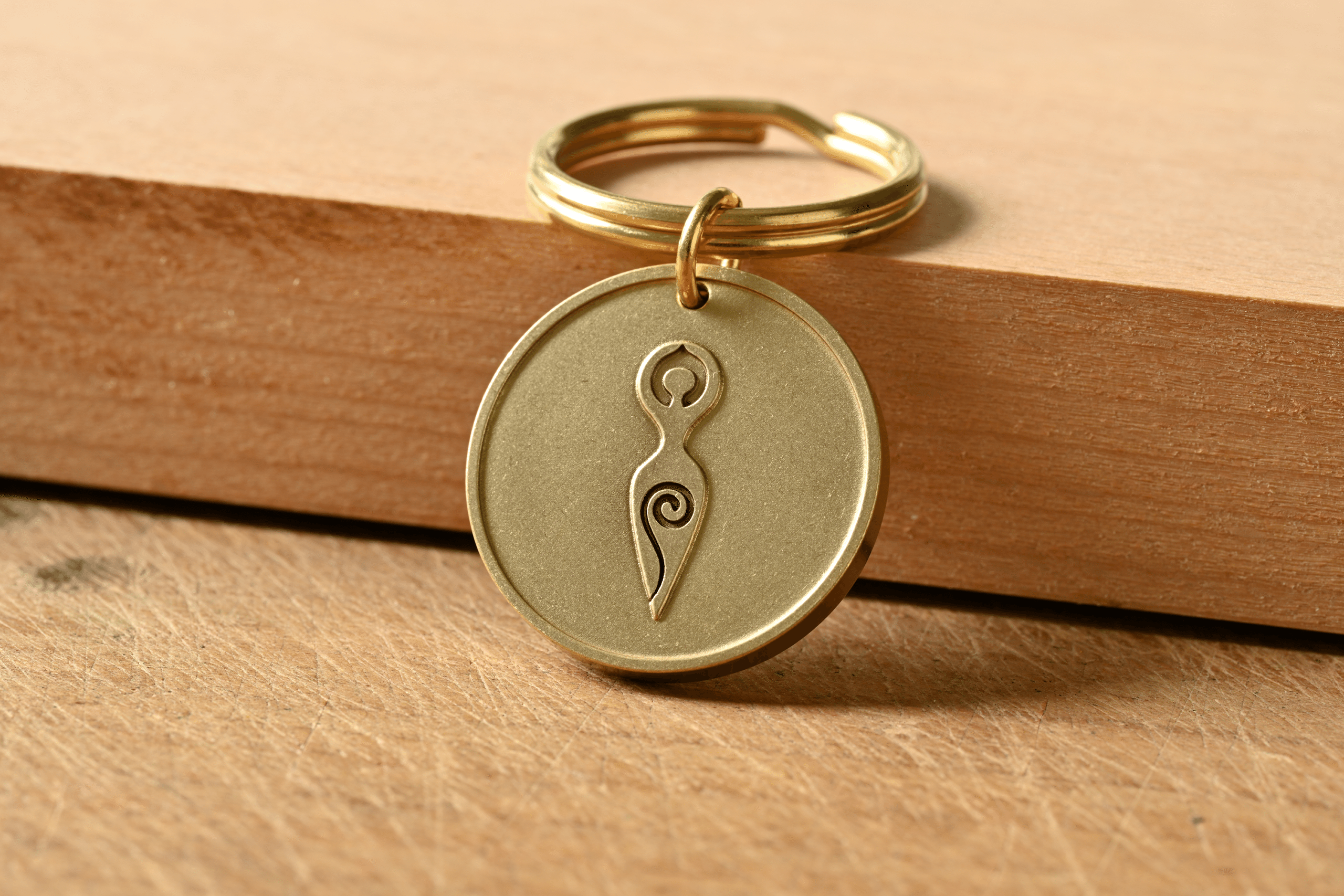 Brass circular keychain engraved with a spiral goddess symbol resting on a wooden surface