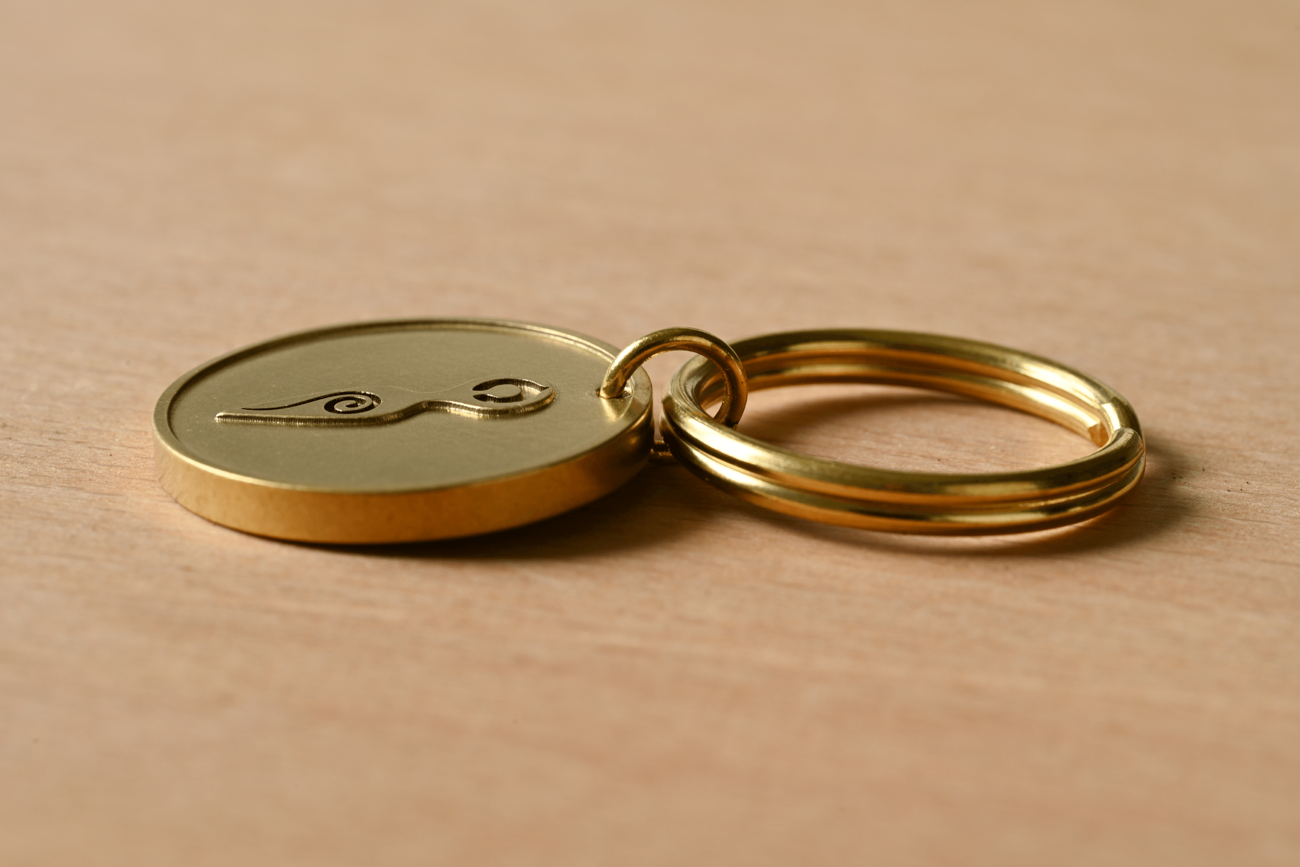 Gold-colored keychain with a round medallion engraved with a stylized symbol on a light wood surface