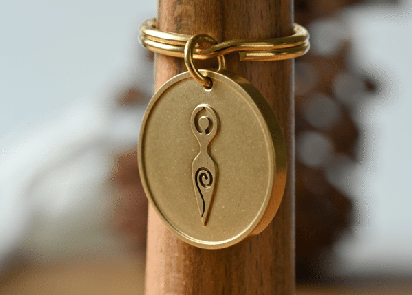 Gold round keychain featuring an embossed spiral goddess symbol