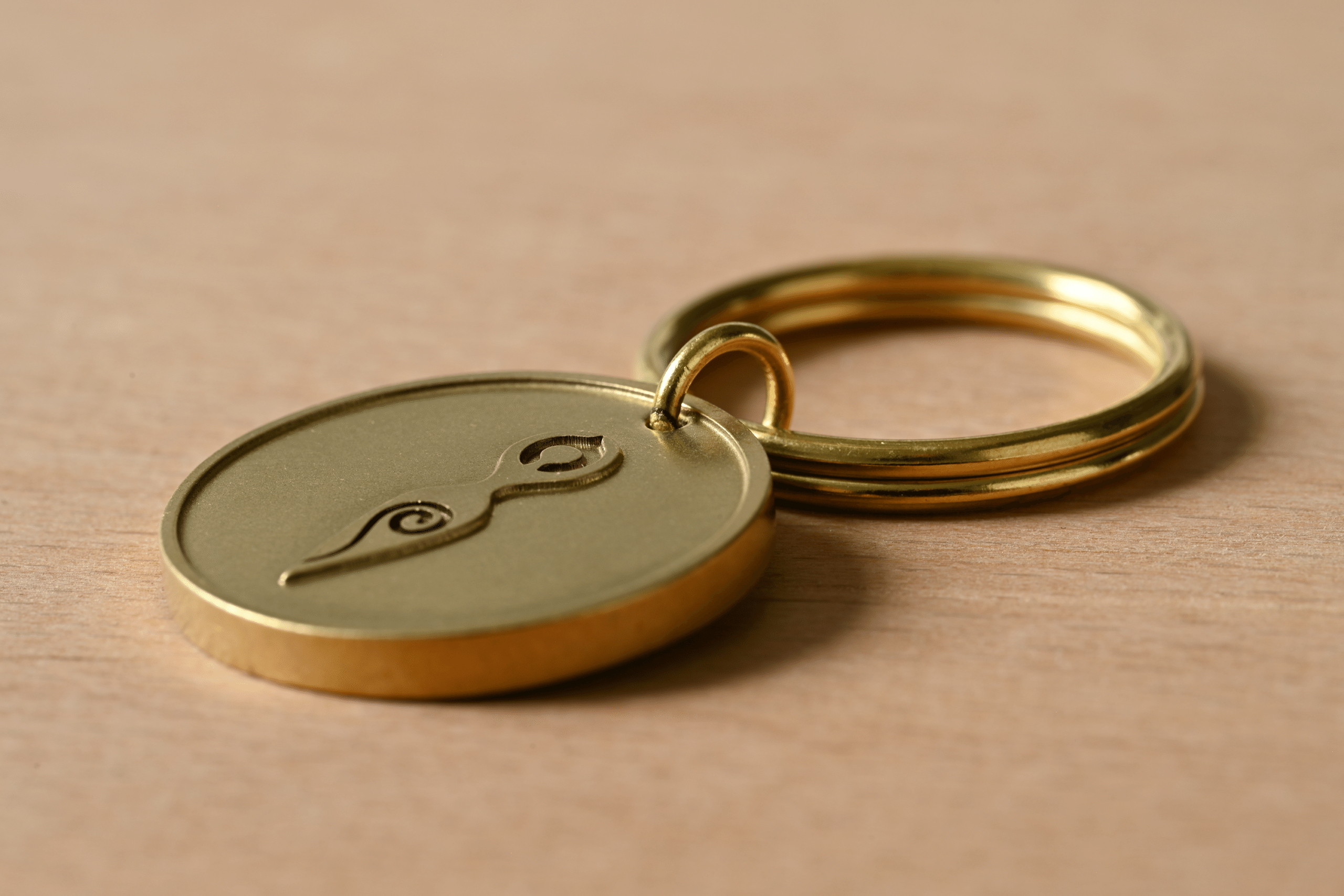 Gold keychain with a circular charm embossed with a stylized goddess symbol and spiral