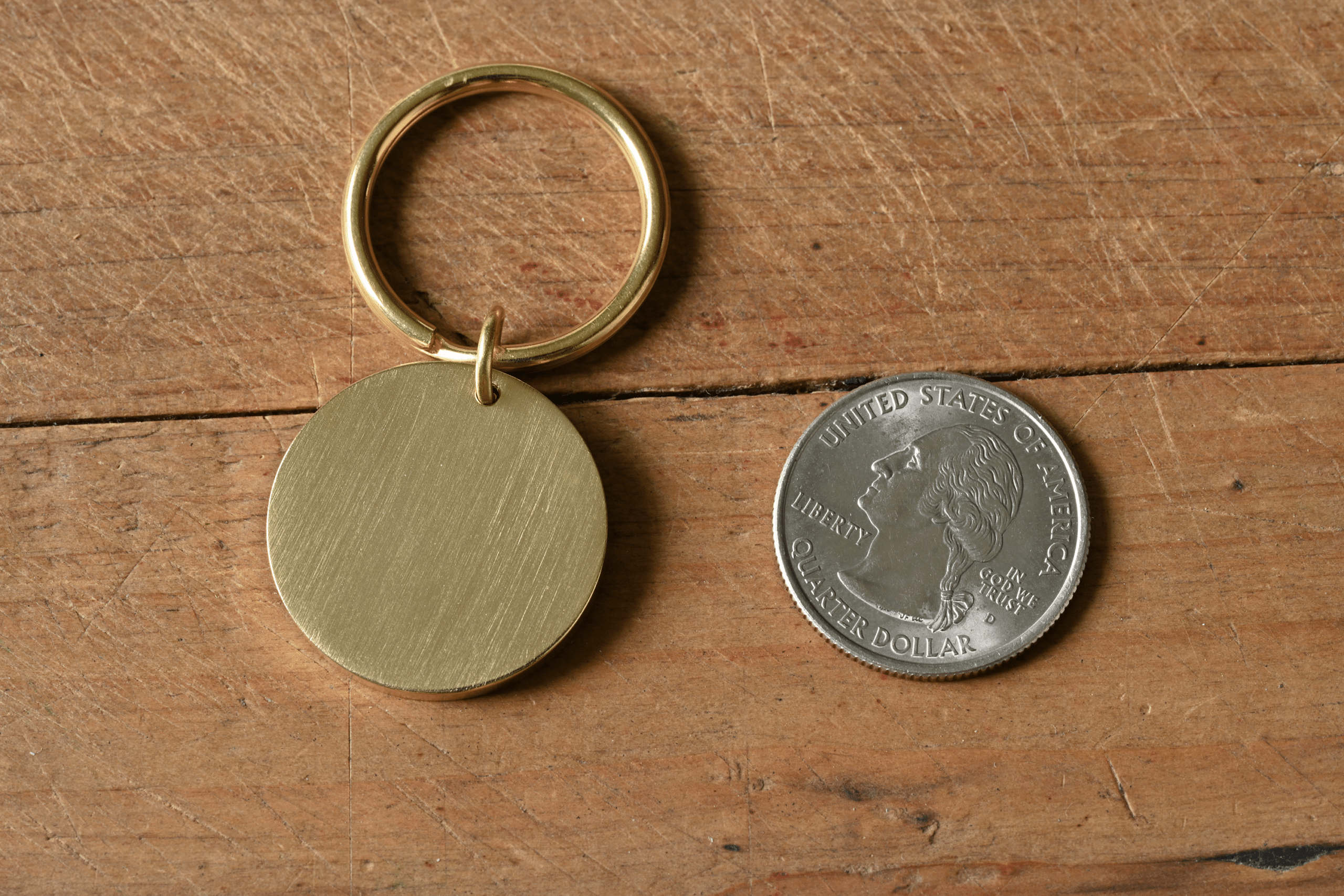 A circular brass keychain tag next to a US quarter for scale