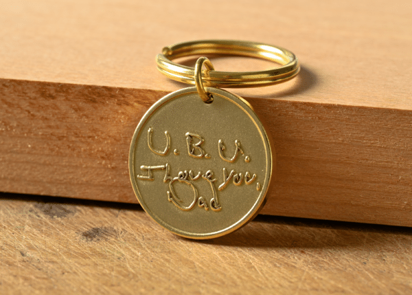 Gold round keychain tag engraved with handwritten text reading U.B.U. I Love You, Dad