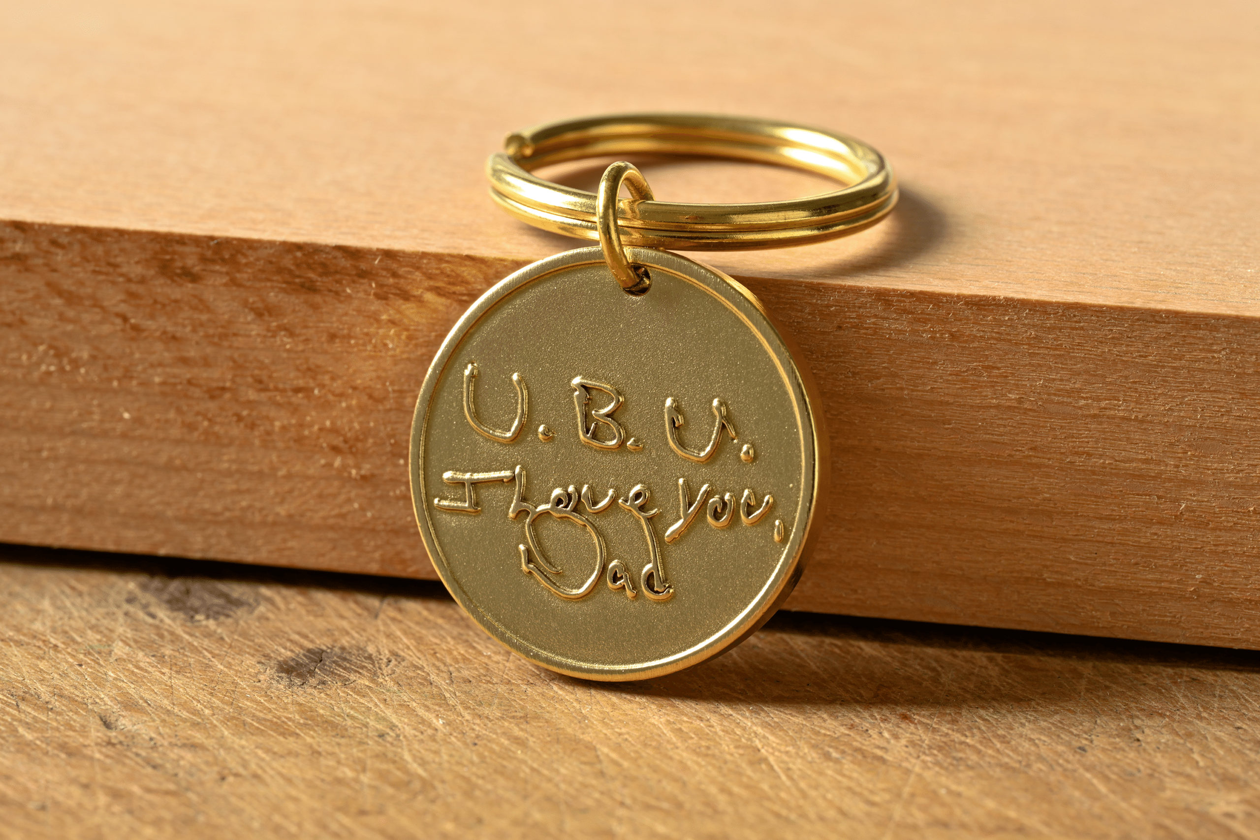 Gold round keychain tag engraved with handwritten text reading U.B.U. I Love You, Dad