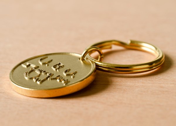Gold round keychain tag engraved with U. B. U. I Love You Dad resting on a wooden surface