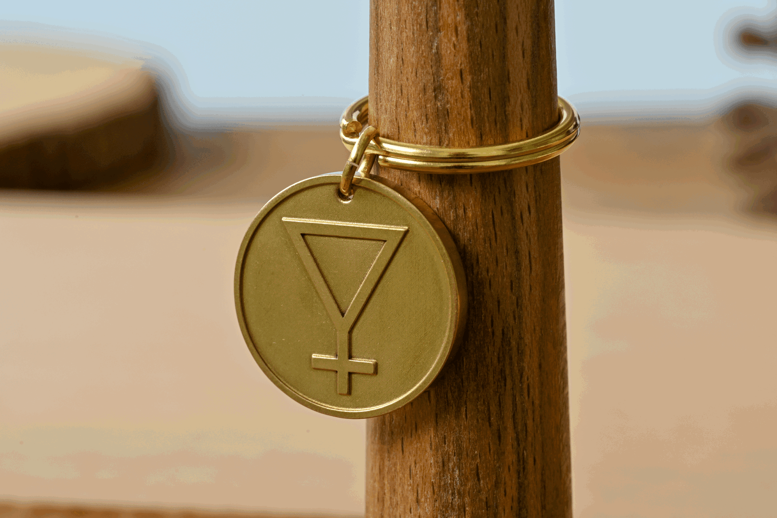 Gold circular pendant engraved with an inverted triangle and cross symbol on a wooden stand
