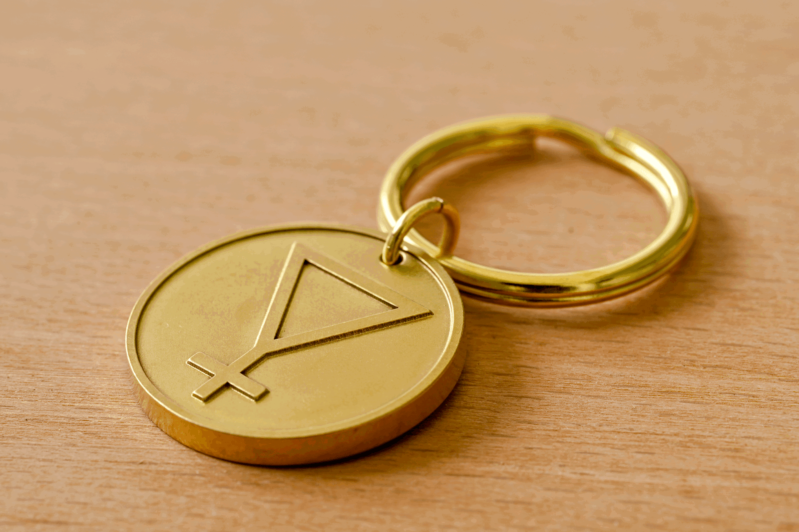 Gold metal keychain pendant engraved with an alchemical symbol, resting on a wooden surface