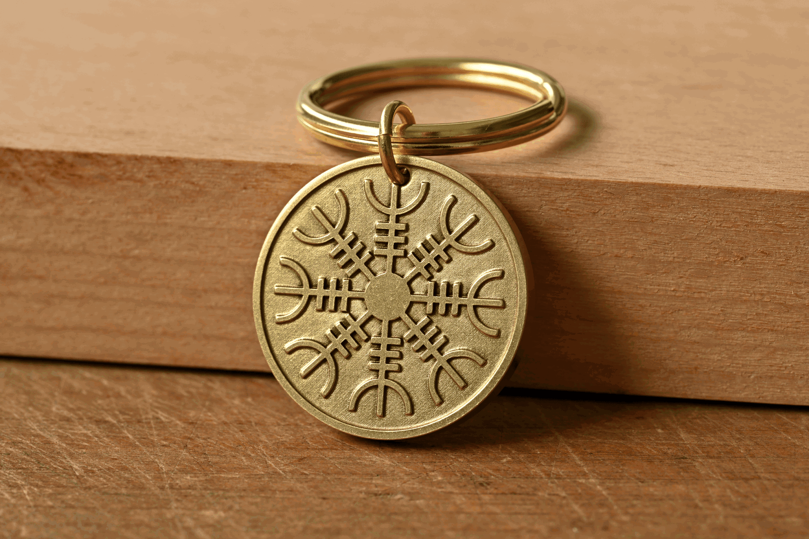 Brass keychain with an engraved Aegishjalmur symbol resting on a wooden block