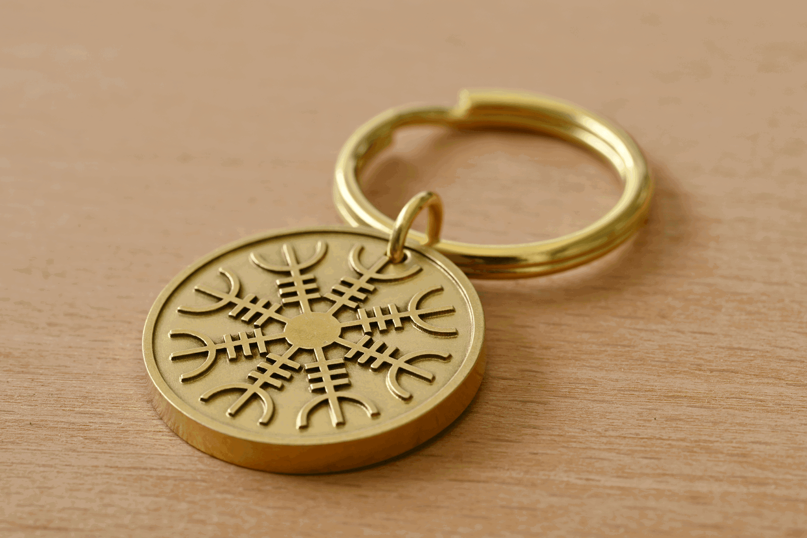 Gold brass keychain with a circular medallion featuring the Helm of Awe symbol on a wooden surface