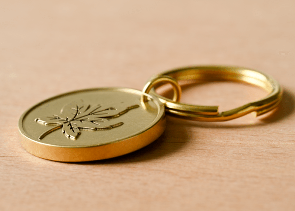 Gold brass keychain with a circular tag engraved with a leaf on a wooden surface