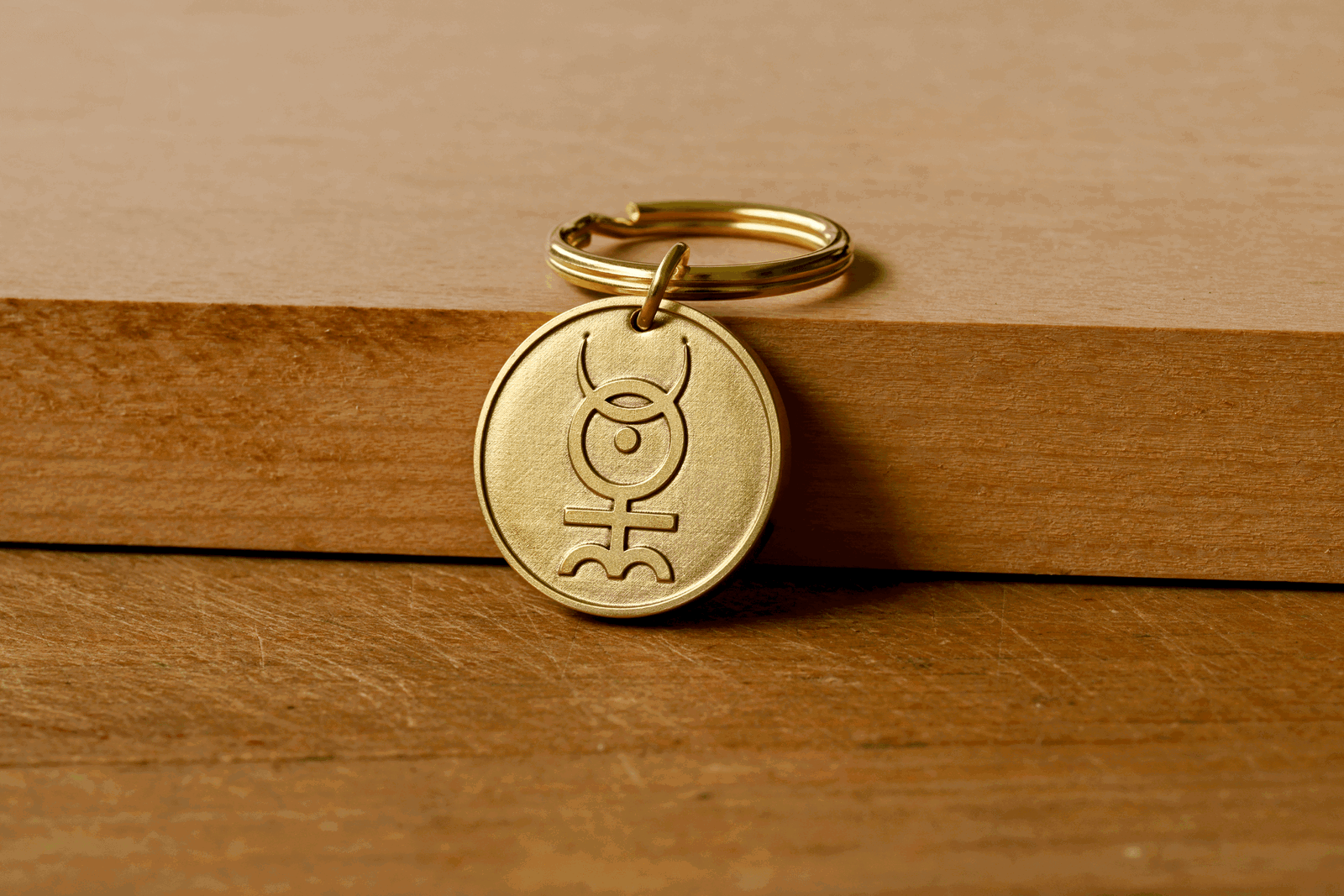 Brass keychain featuring an engraved Monas Hieroglyphica symbol resting on a wooden surface