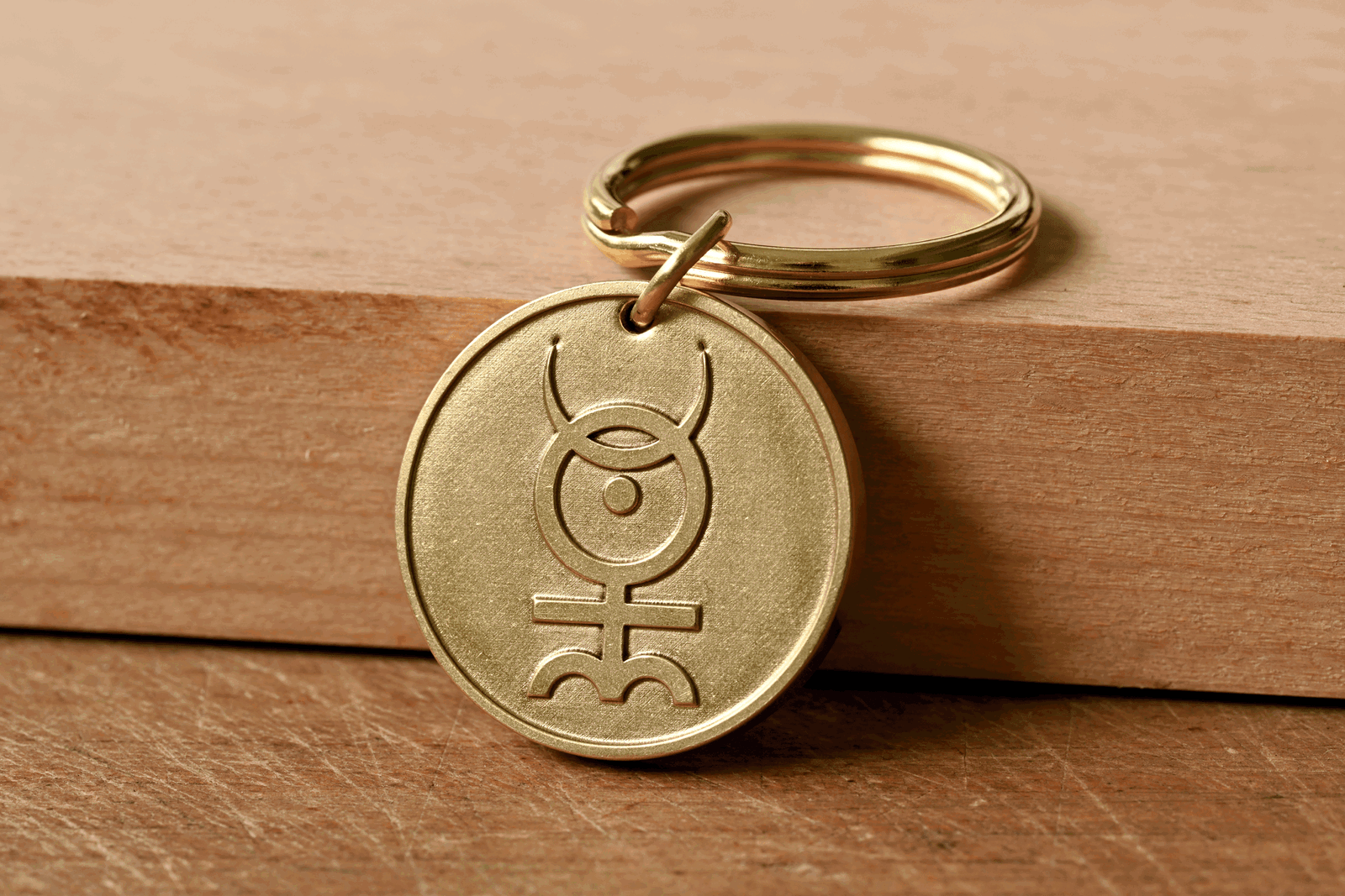 Brass key ring medallion engraved with the Monas Hieroglyphica symbol, resting against a wooden block