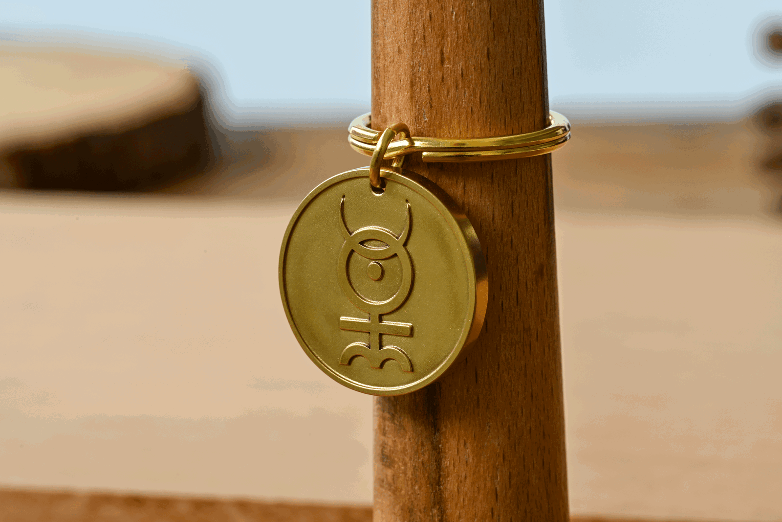 Gold brass keychain tag engraved with an alchemical symbol, displayed on a wooden post