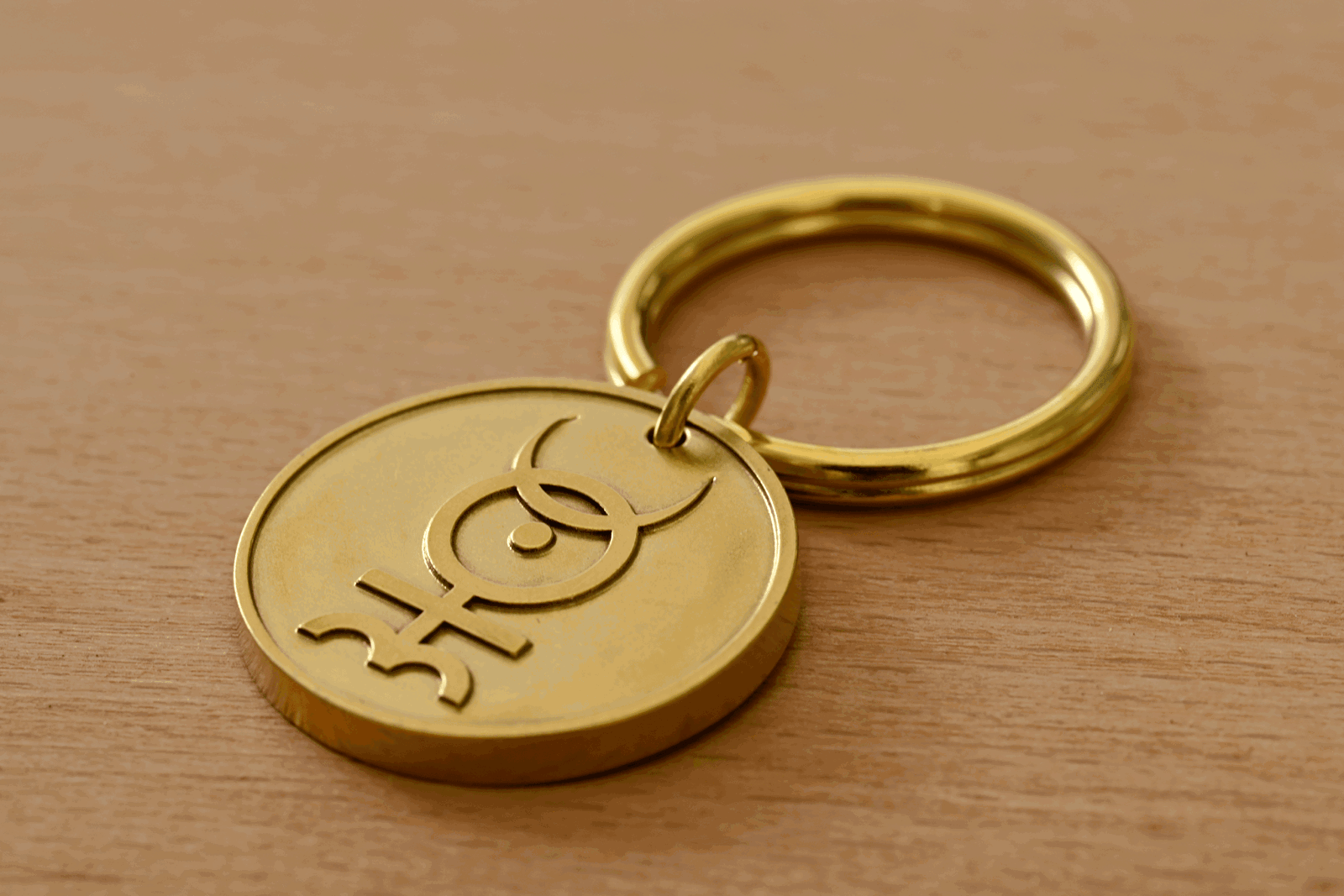 Gold keychain featuring a circular medallion engraved with an astrological symbol, resting on a wooden surface