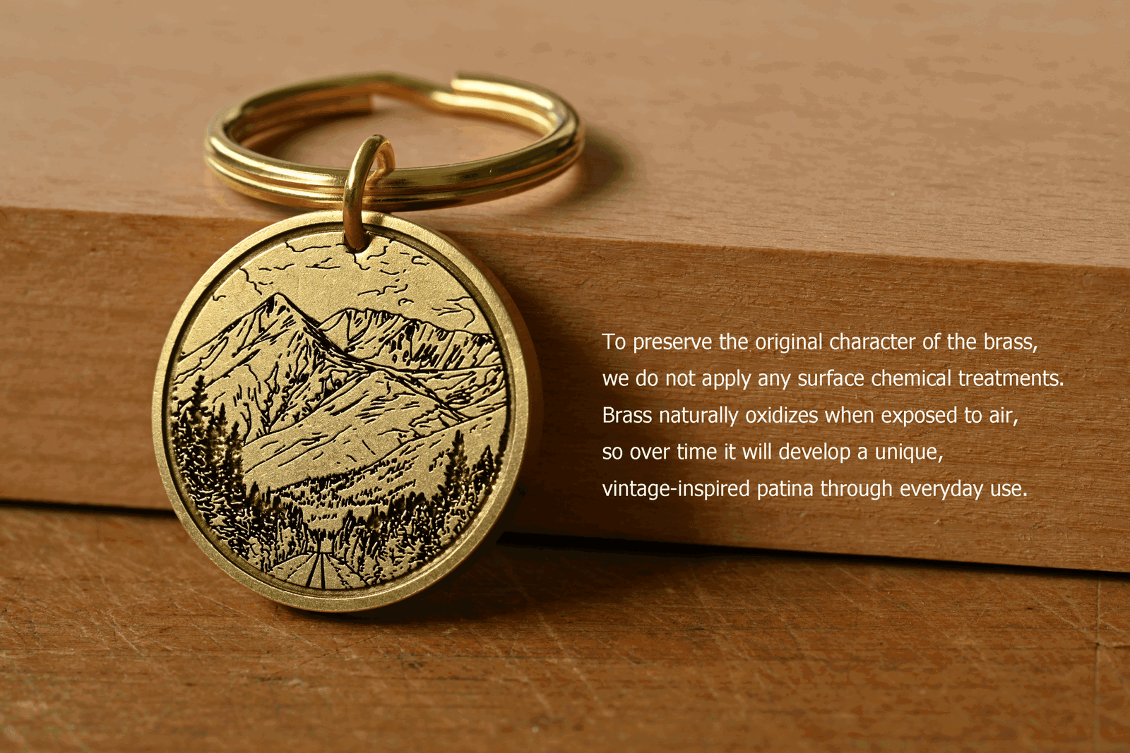 Brass keychain engraved with a mountain scene next to text that reads: To preserve the original character of the brass, we do not apply any surface chemical treatments. Brass naturally oxidizes when exposed to air, so over time it will develop a unique, vintage-inspired patina through everyday use