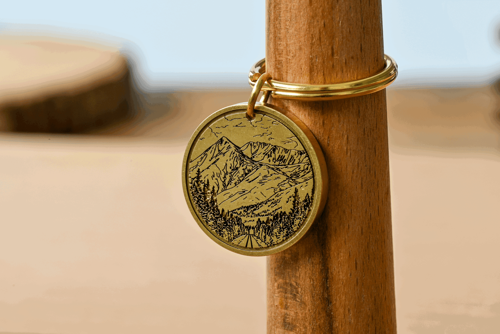 Engraved brass keychain featuring a mountain landscape with pine trees and a road